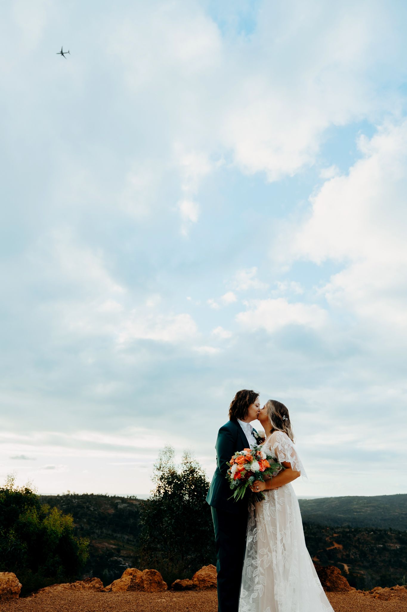 A couple shares a romantic moment during their mountaintop wedding ceremony against a scenic autumn landscape.