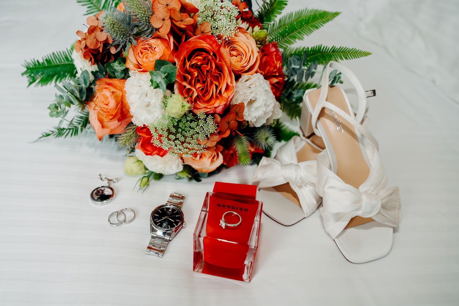 Coral and peach roses arranged with greenery and silver ornaments on a light gray surface.