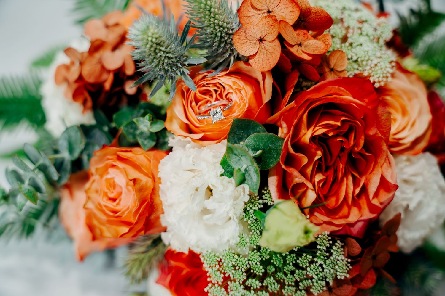 A vibrant wedding bouquet featuring orange roses, white flowers, and delicate green foliage arranged in a romantic style.