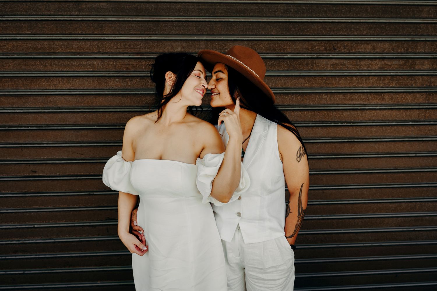 Two people in wedding attire share tender moments against a corrugated metal backdrop.