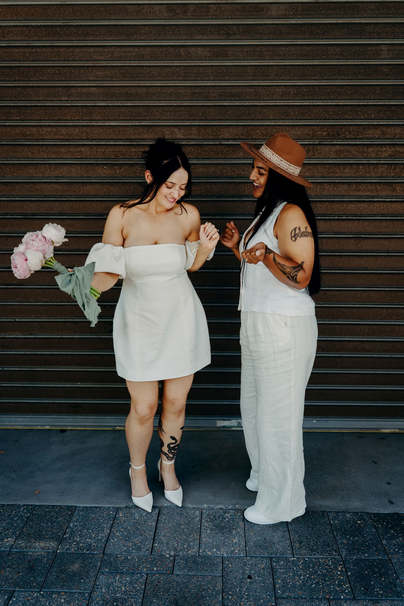 Two people wearing white towels pose playfully against a metal security gate background.
