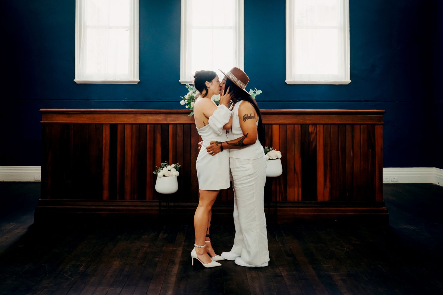 Elegant ballroom dancers dressed in white dance together during practice in a dark studio with wooden floors and mirrors.