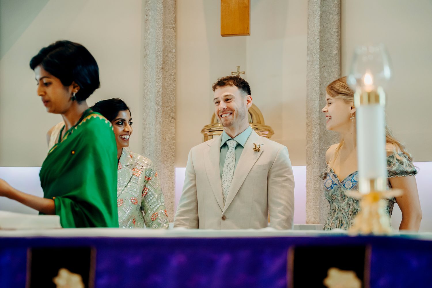 Wedding party stands at altar during church ceremony with candlelit decor in background.