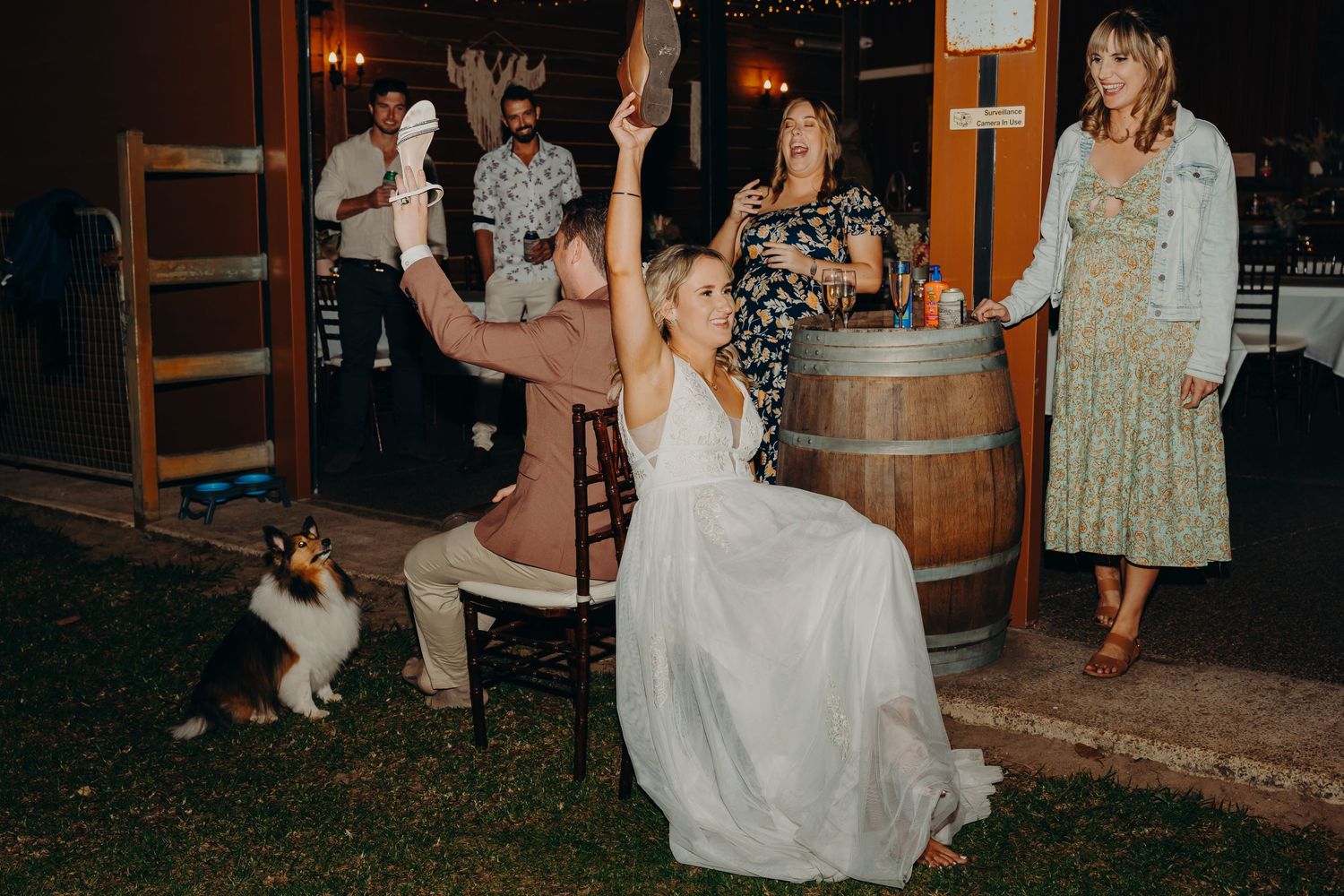 Celebratory moment at rustic outdoor wedding reception with wine barrels and string lights.