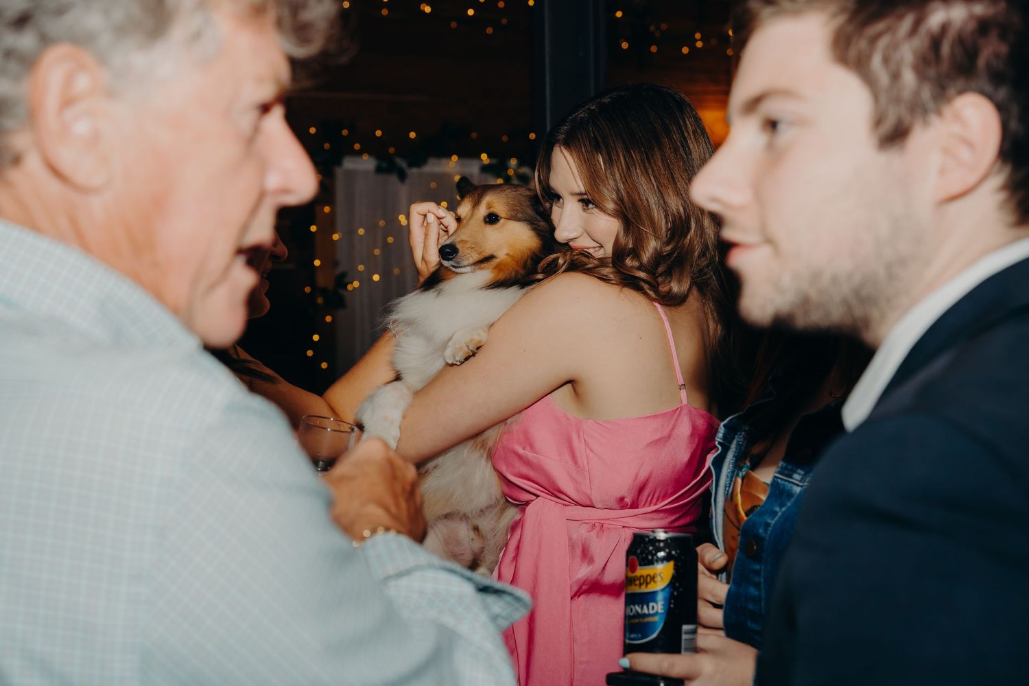 Small dog being held during wedding reception conversation.