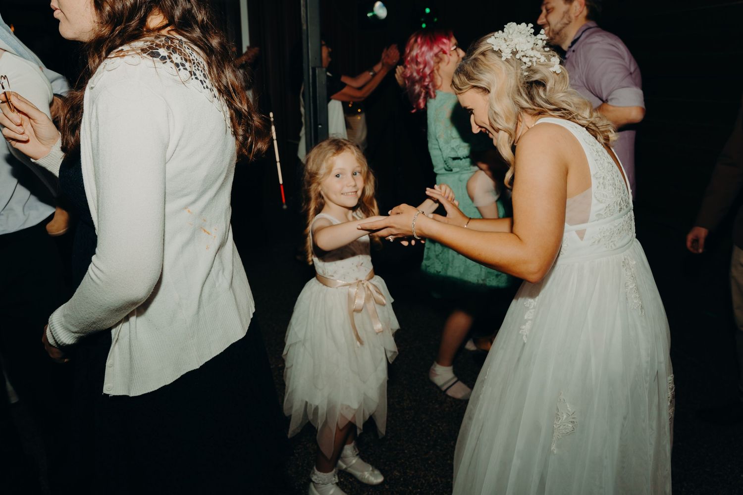 A bride dances with a young flower girl in a tulle dress during a wedding reception.