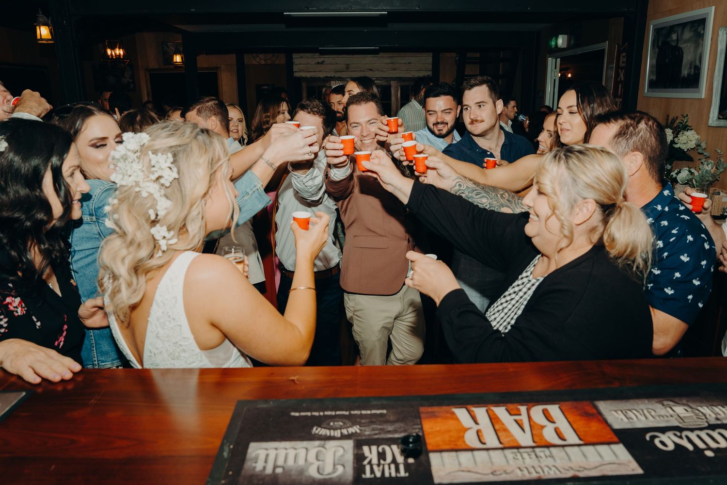 Wedding guests raising glasses in a celebratory toast at a bar reception.