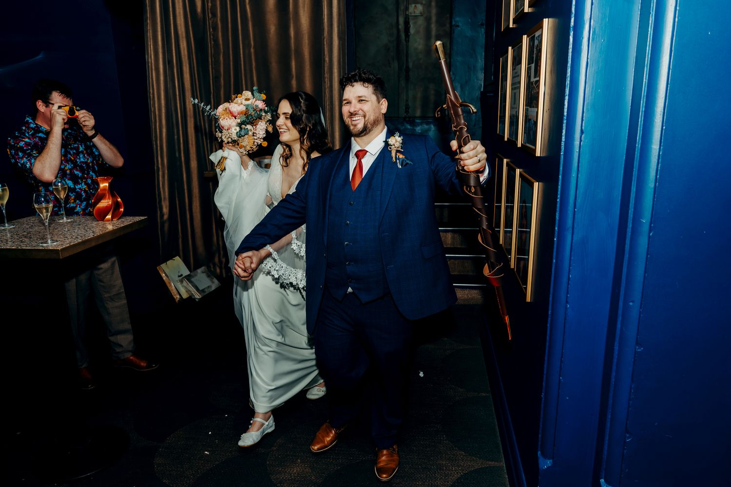 Wedding guests dance and celebrate on a dimly lit dance floor with blue lighting during an evening reception.