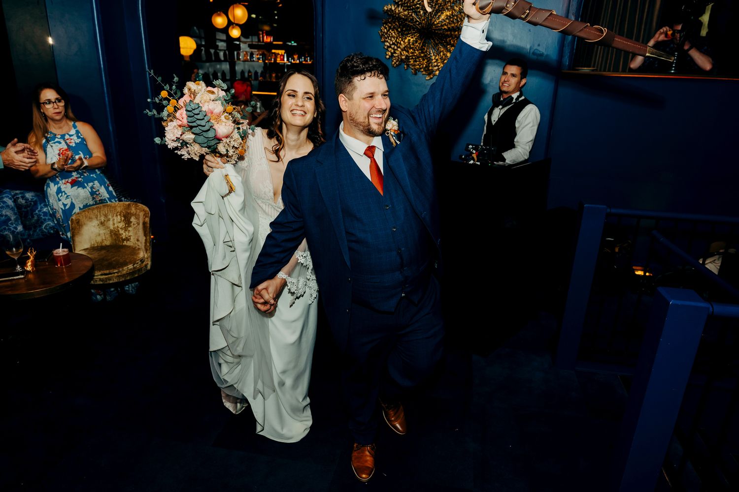 A couple walks through a darkly lit venue decorated with glowing lanterns and elegant furniture.