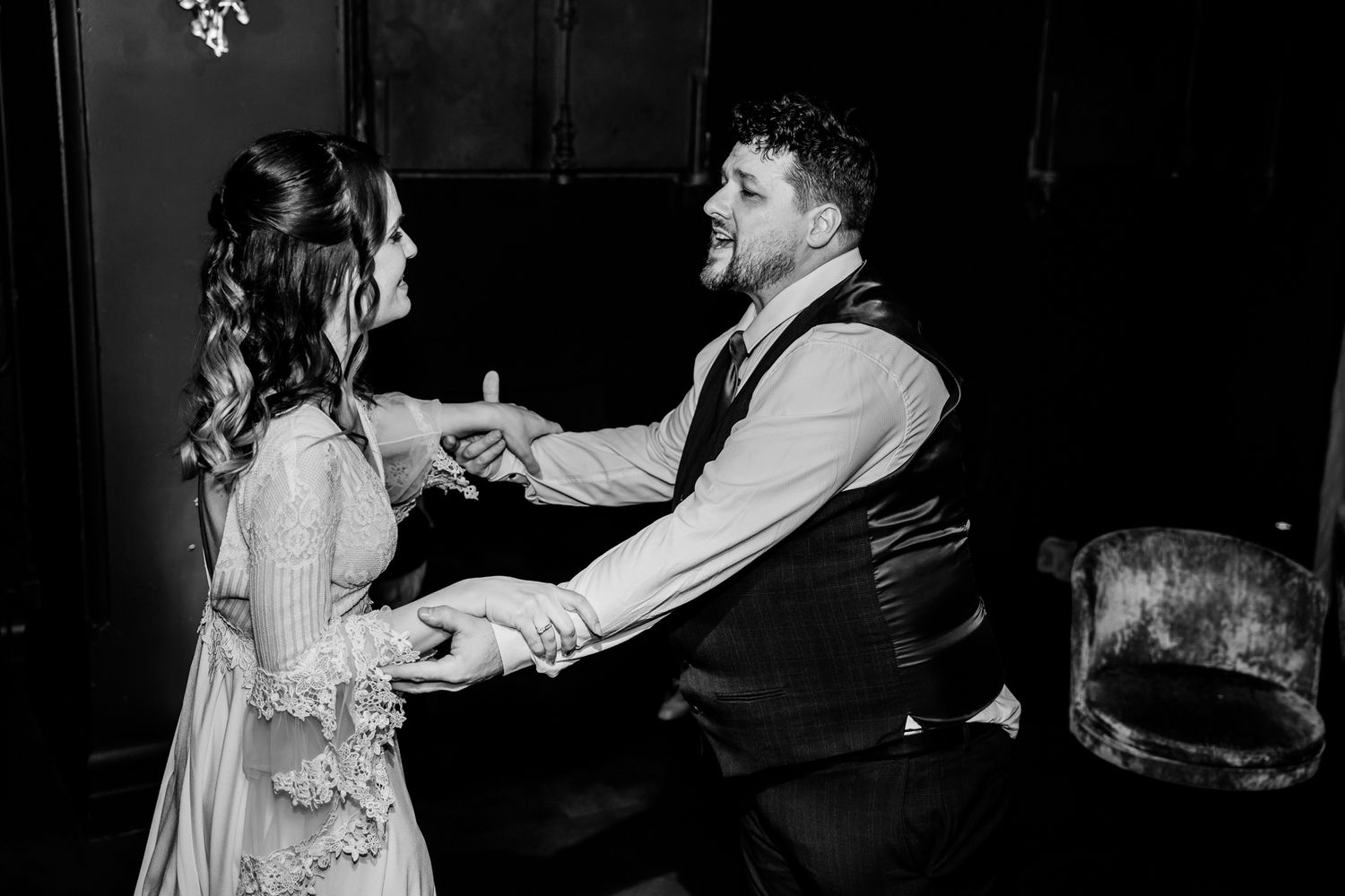 A candid black and white photo of a couple sharing a romantic dance moment at a wedding.