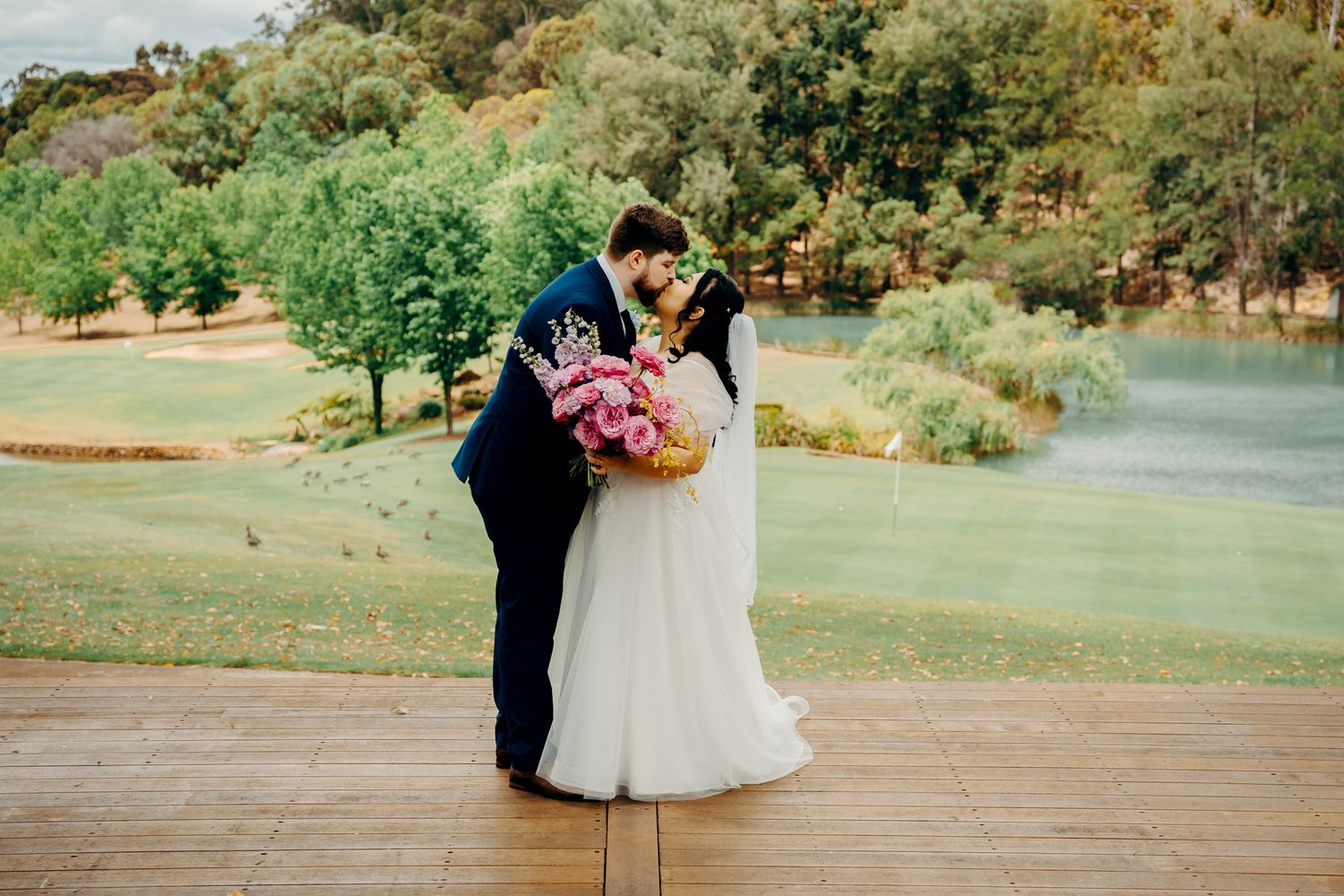 Two figures share an intimate moment on a wooden deck overlooking a scenic countryside with autumn foliage.