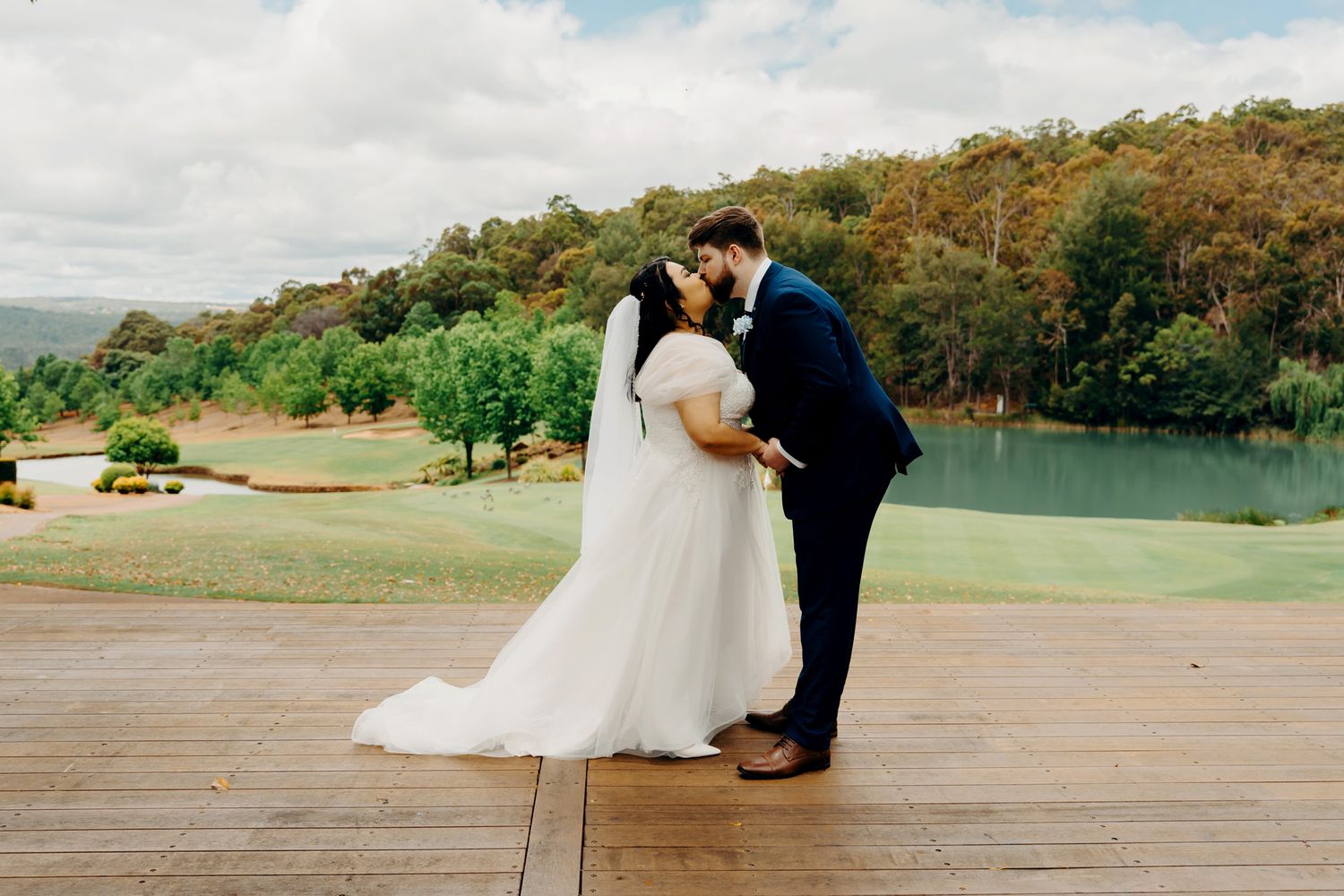 A romantic couple embraces against an autumn landscape of rolling hills and trees at a scenic outdoor wedding venue.
