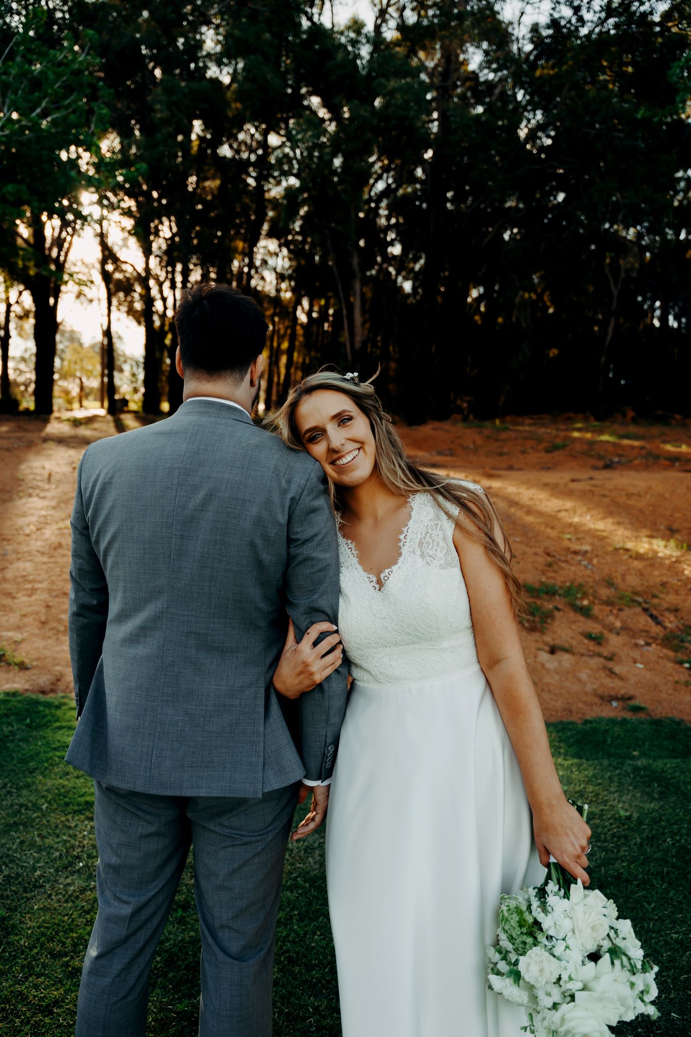 A romantic wedding photo series showing a couple in formal attire walking together on a tree-lined path at sunset.