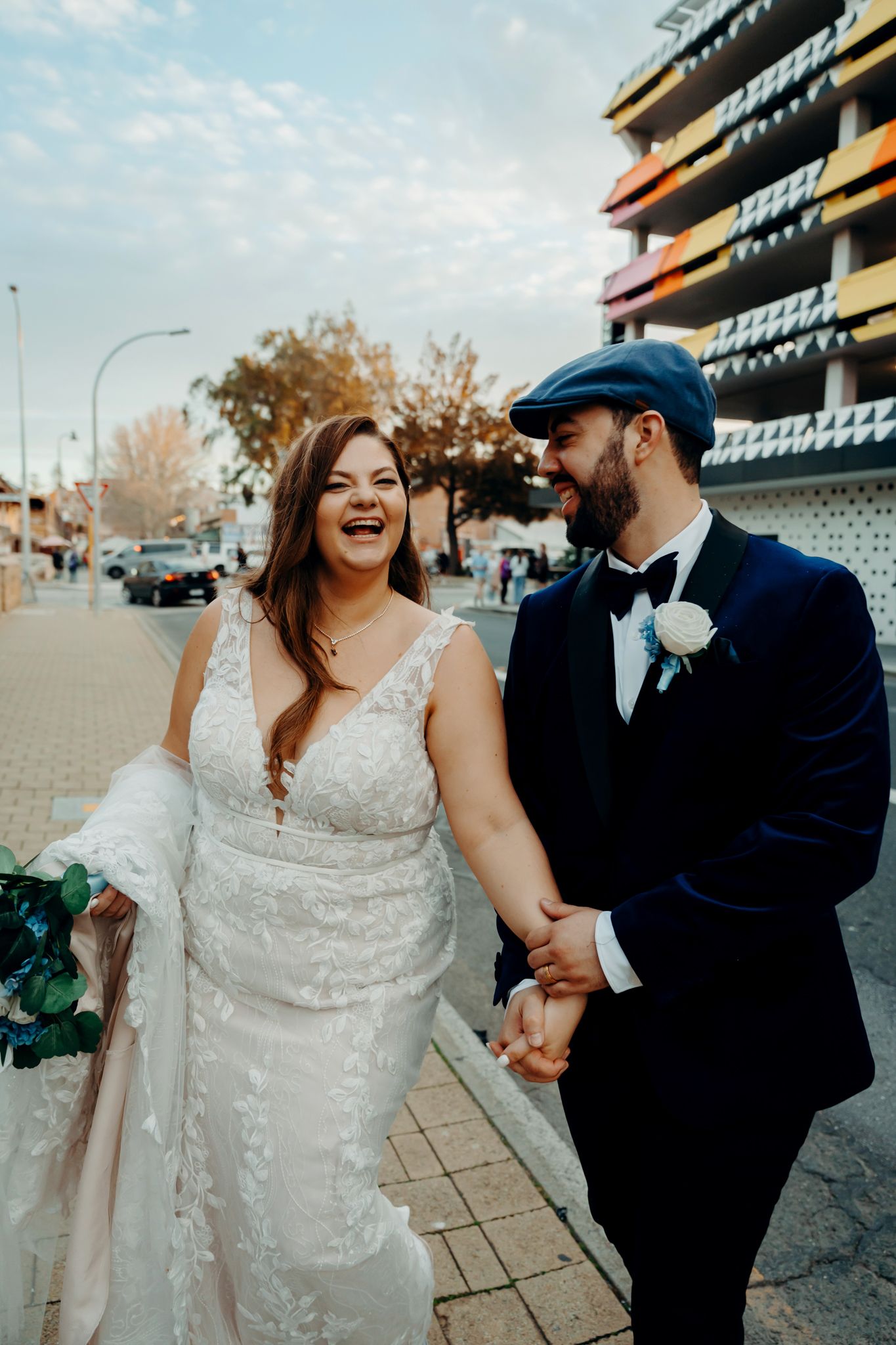 A couple shares joyful moments during their wedding photoshoot outside a stadium on an autumn day.