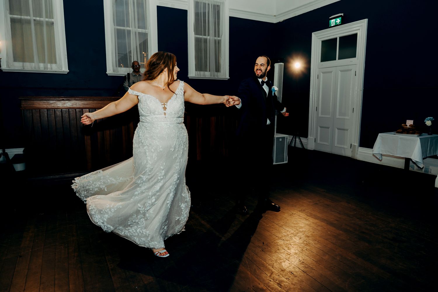 Newlyweds dance together on a polished wooden floor in a dimly lit reception venue.
