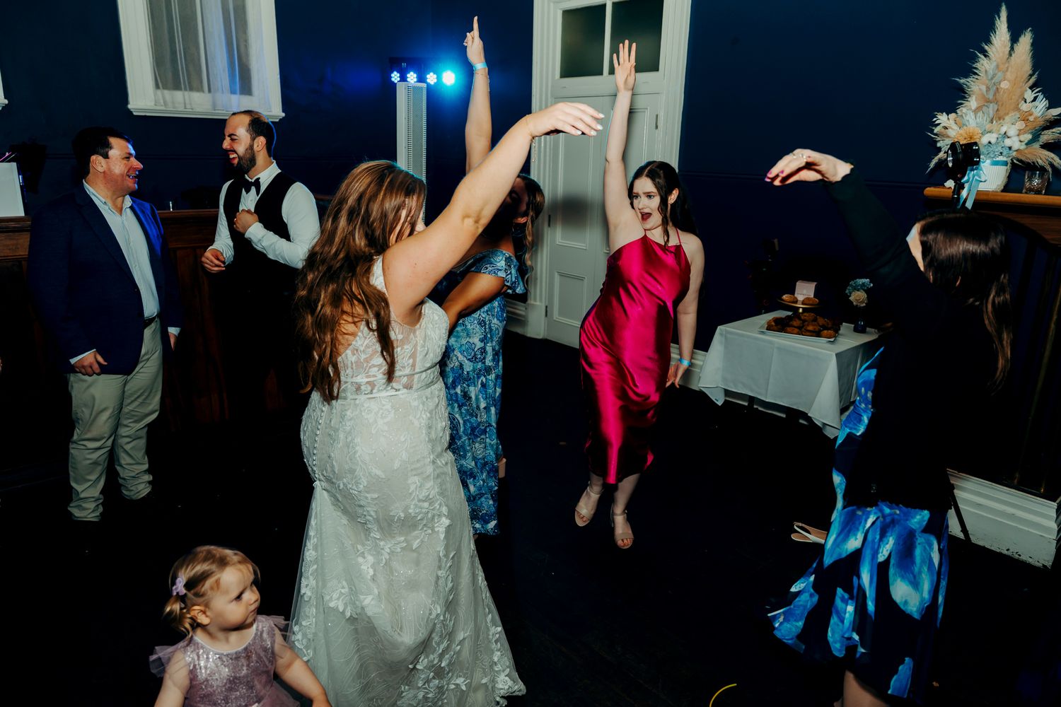 Wedding party dancing and celebrating on a dark wooden dance floor during the reception.