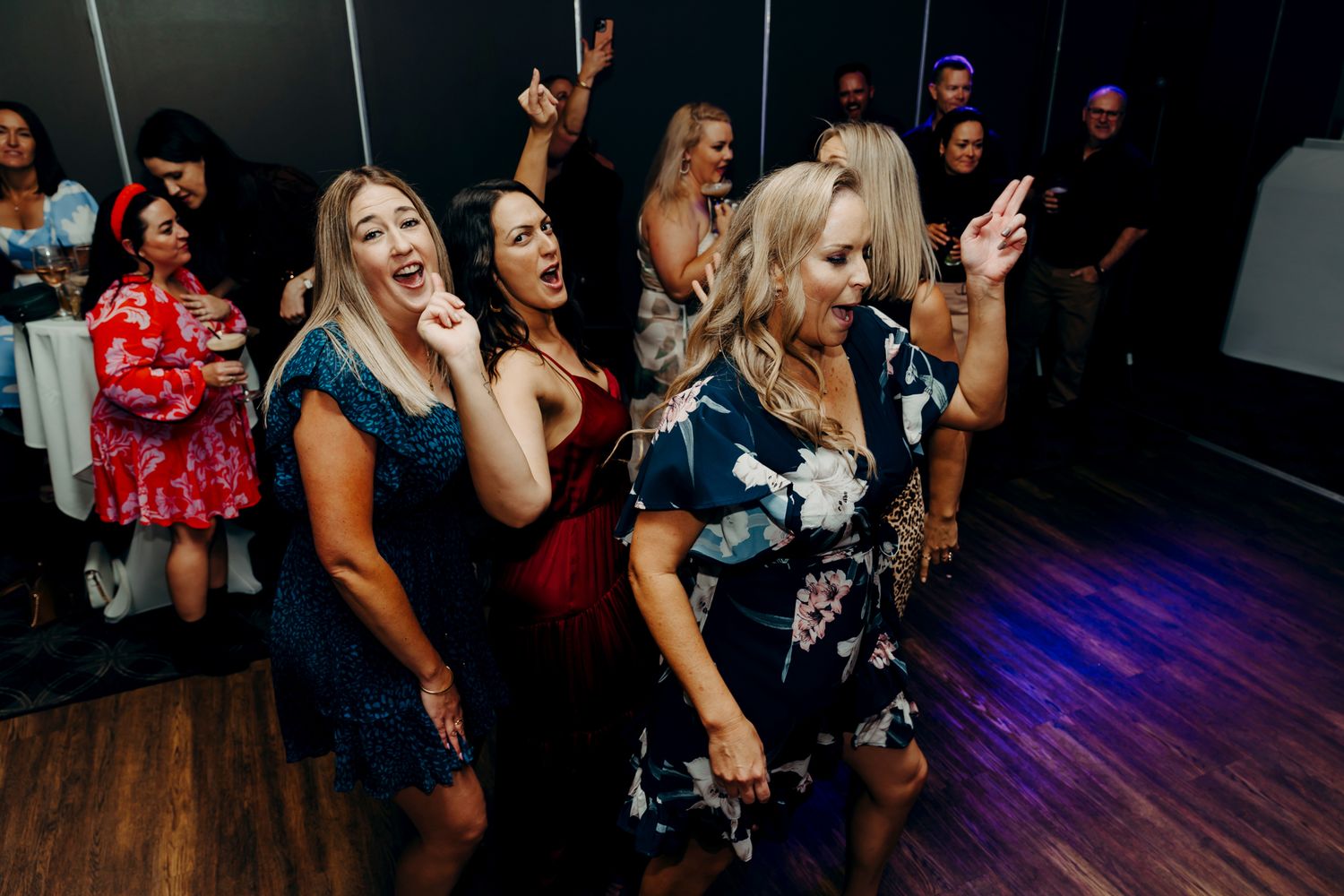 A group of people dancing and celebrating on a dark dance floor with blue lighting in the background.