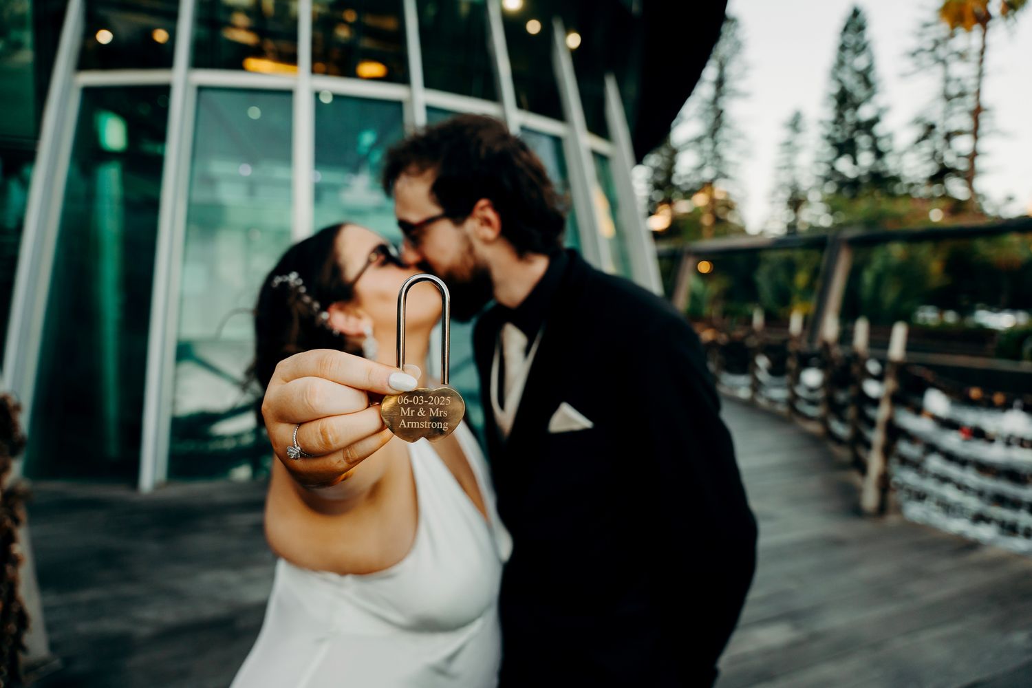 A couple in wedding attire embraces intimately in a romantic winter setting with evergreen trees and snow.