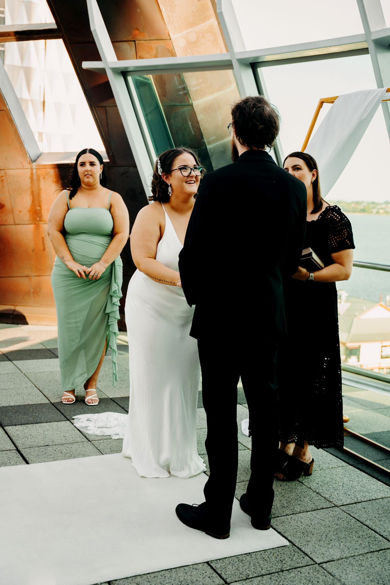 A tender wedding moment of people in formal attire embracing in front of bright windows and doors.