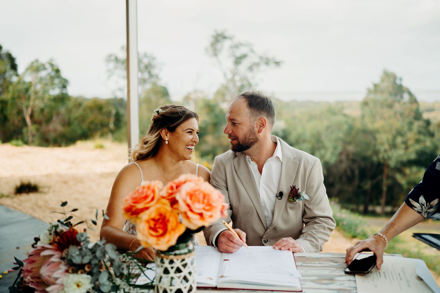A couple in wedding attire shares a romantic moment in a scenic outdoor setting at sunset.
