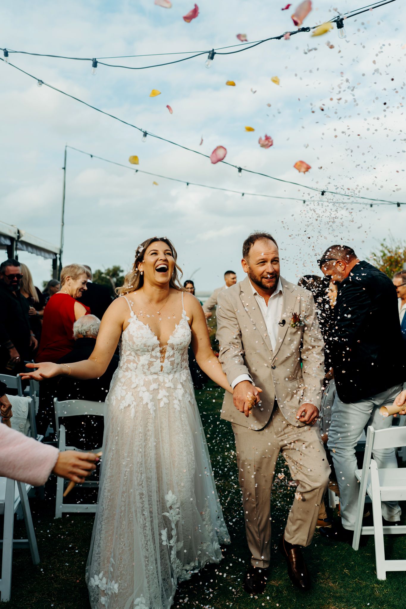 Wedding celebration with colorful confetti being thrown over a couple and guests during an outdoor ceremony.