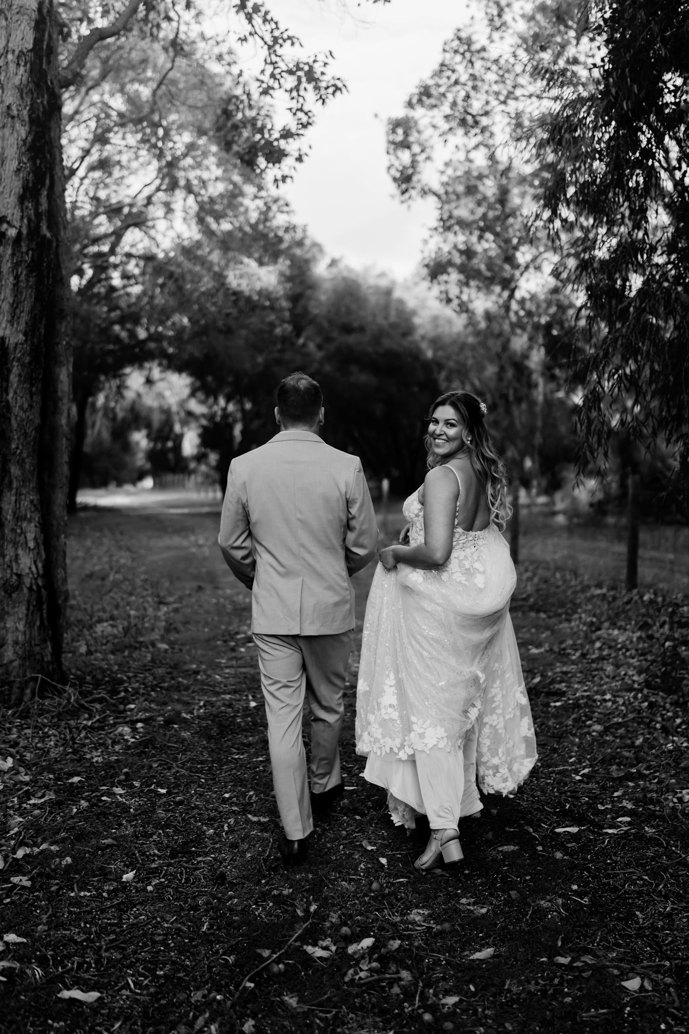 A couple walks through a wooded area in black and white, creating a romantic silhouette against the trees.