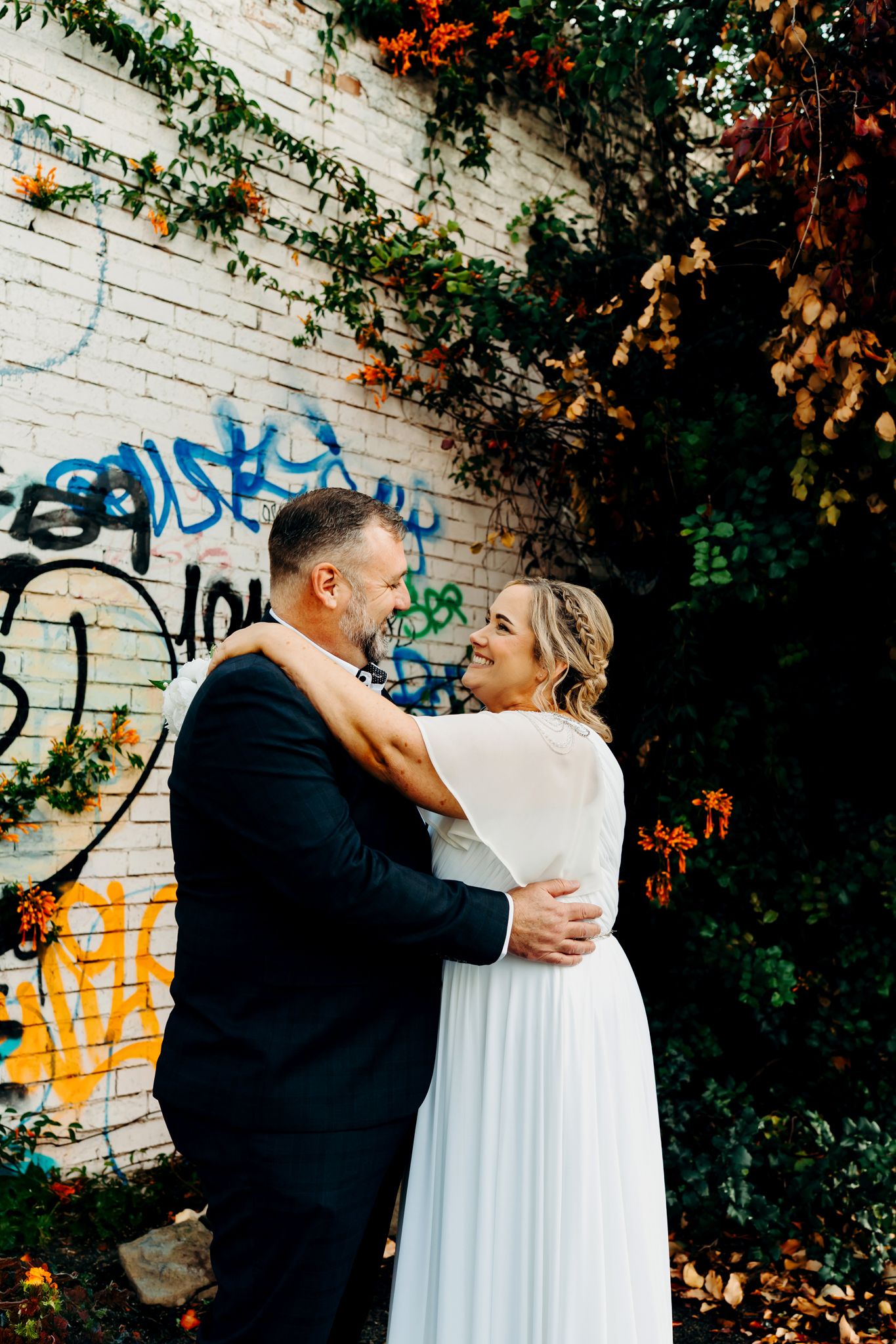 Couple shares romantic embrace in front of graffiti wall with autumn foliage adding vibrant color to urban backdrop.