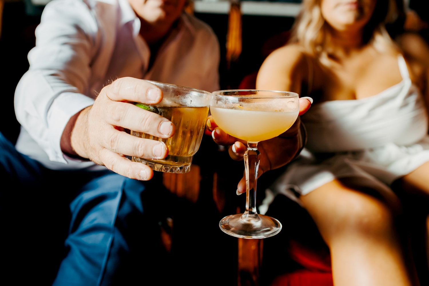 Two hands hold colorful cocktail glasses during a social gathering at a bar or restaurant.