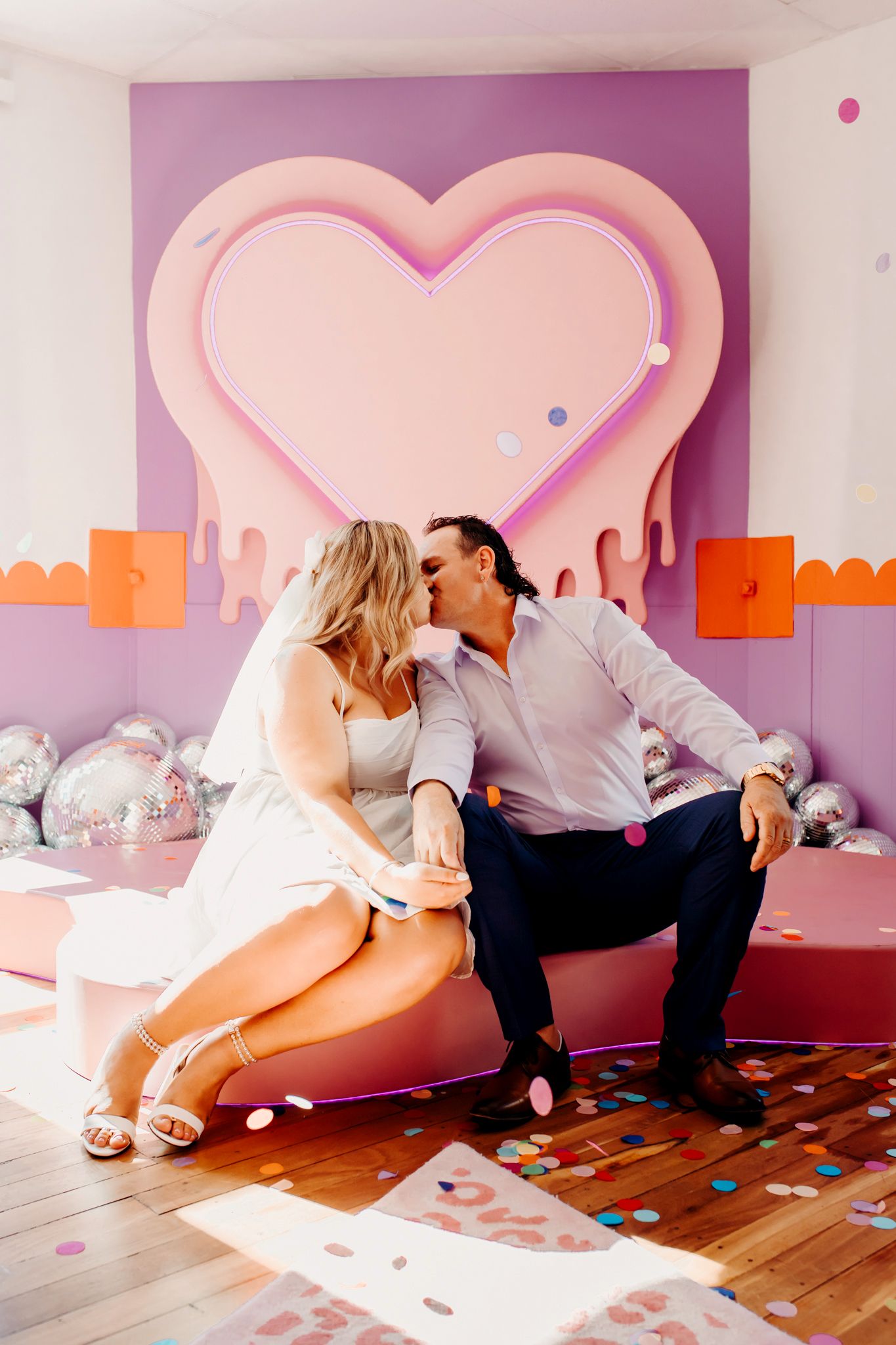 A romantic scene with a pink heart backdrop and decorative silver balloons on wooden flooring in pastel colors.