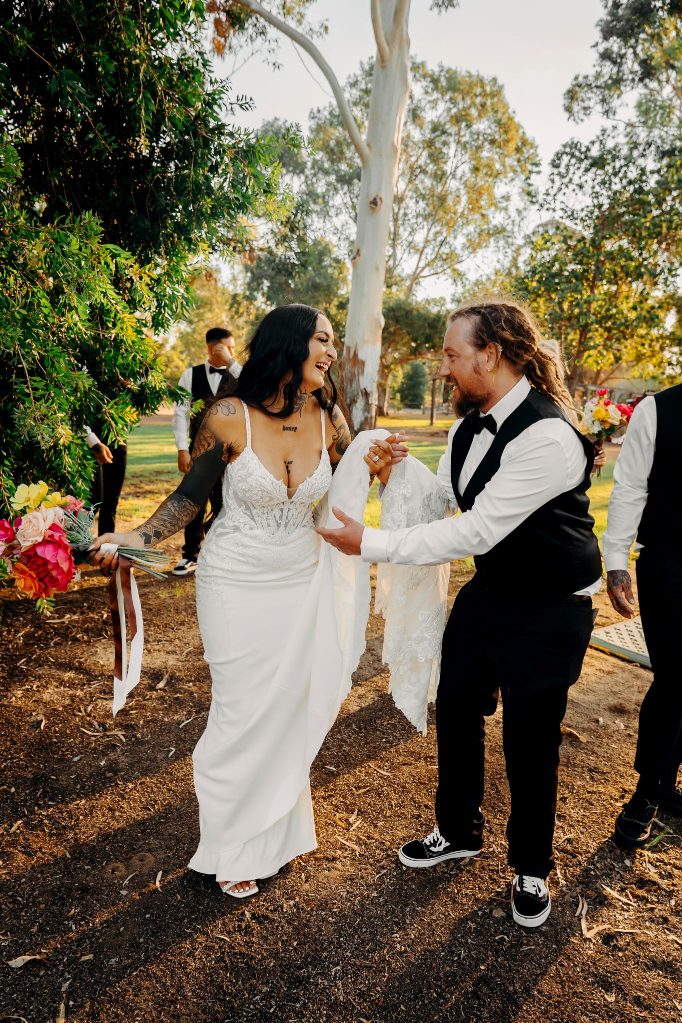 A couple dances together on rustic outdoor grounds with tall eucalyptus trees in the background.