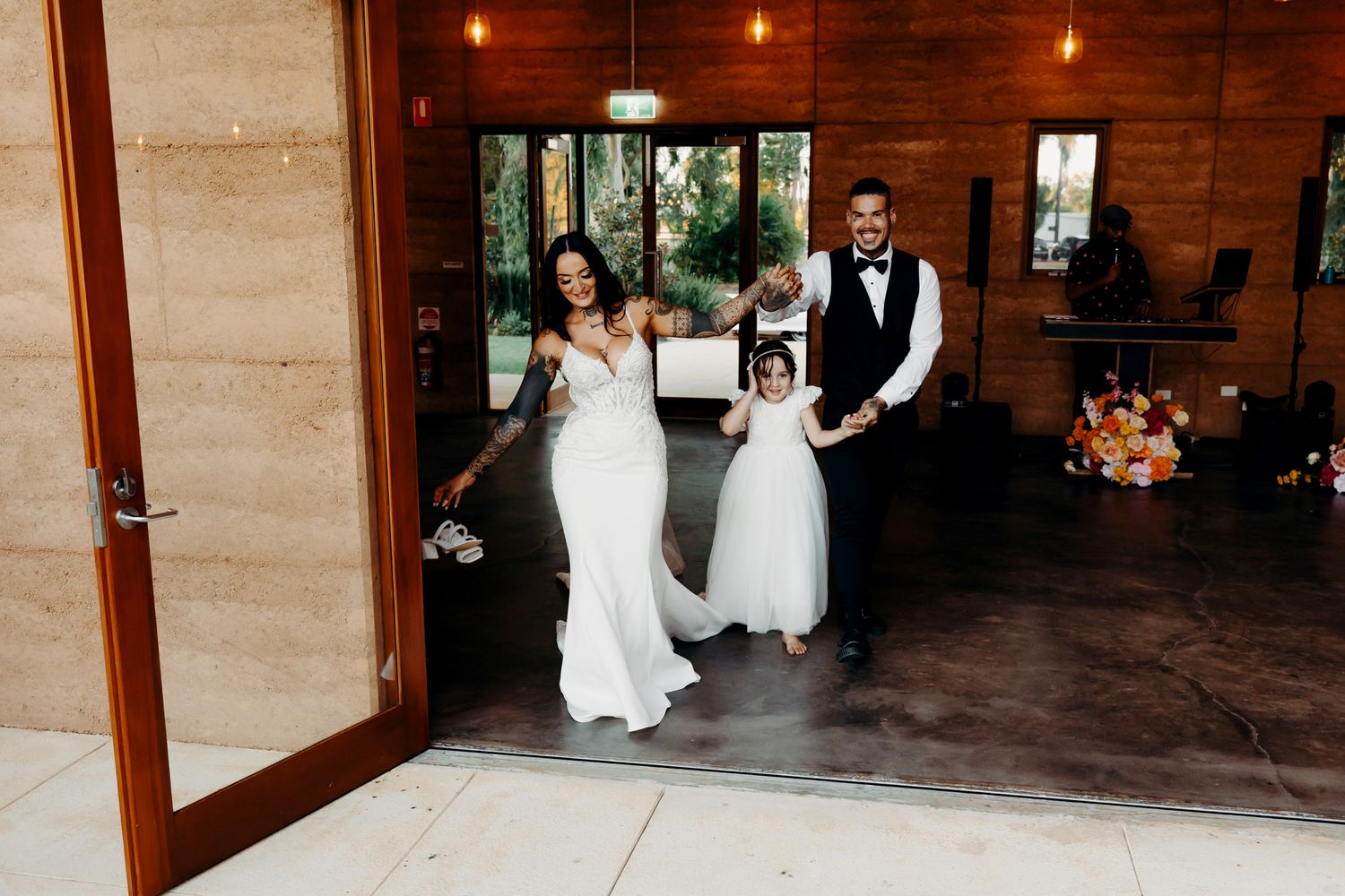 Wedding party enters a rustic wooden venue through large glass doors.
