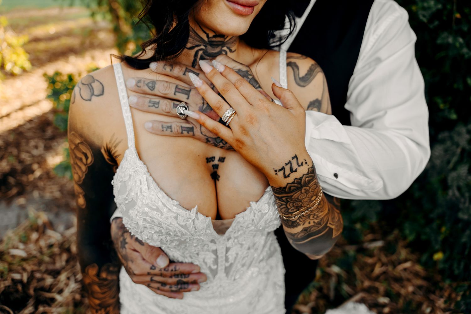A close-up view of a couple's hands touching tenderly while wearing elegant wedding attire in an outdoor setting.