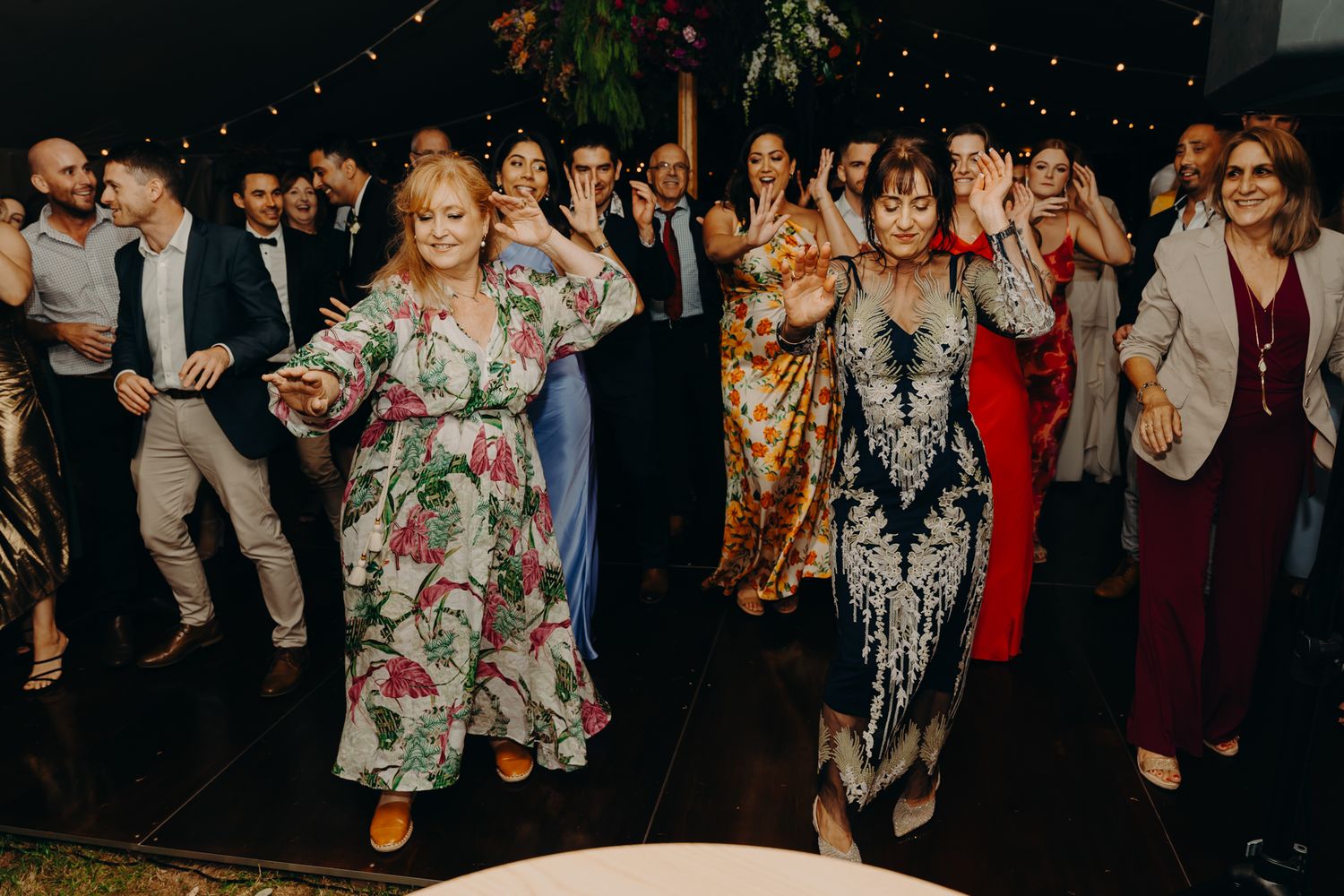 Wedding guests dancing and celebrating at indoor reception with string lights.