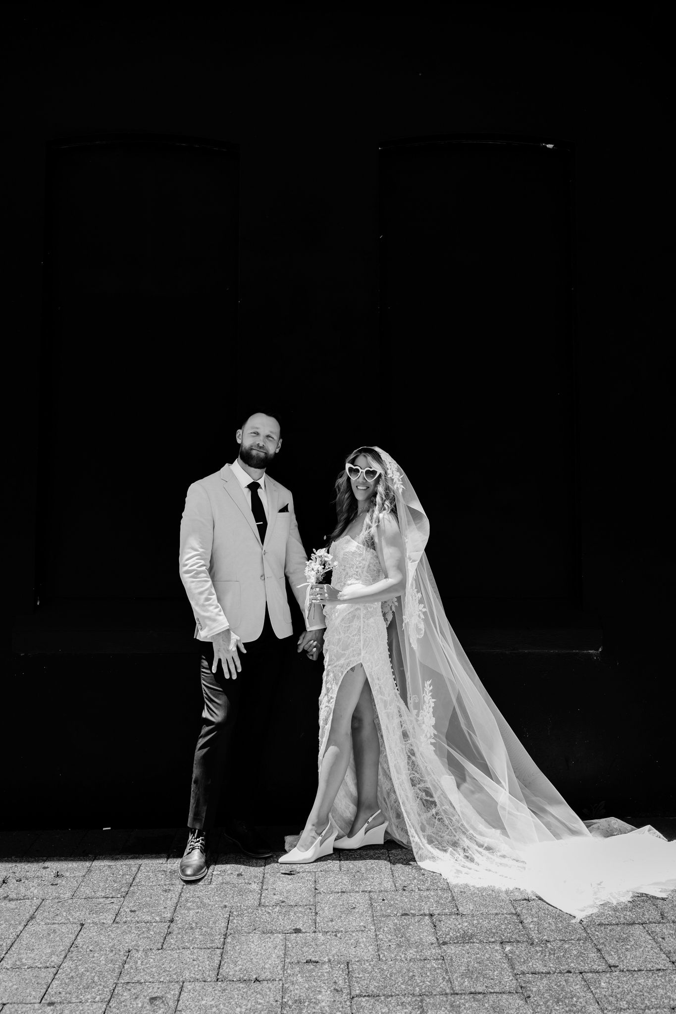 A black and white wedding photo series showing a couple in formal attire walking and posing on stone pavement.