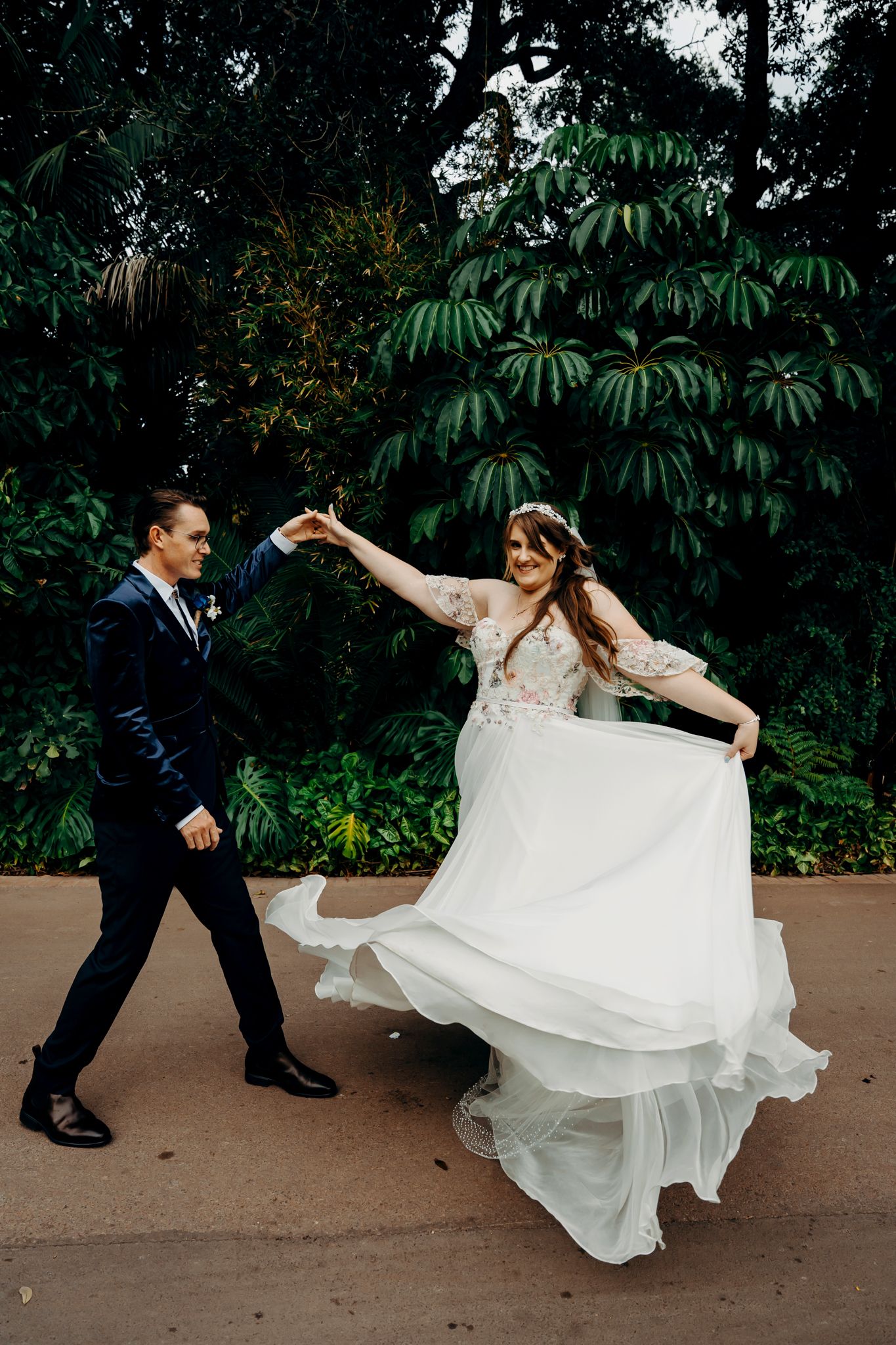 A dance sequence shows a couple performing playful spinning movements in formal wedding attire on a paved pathway.
