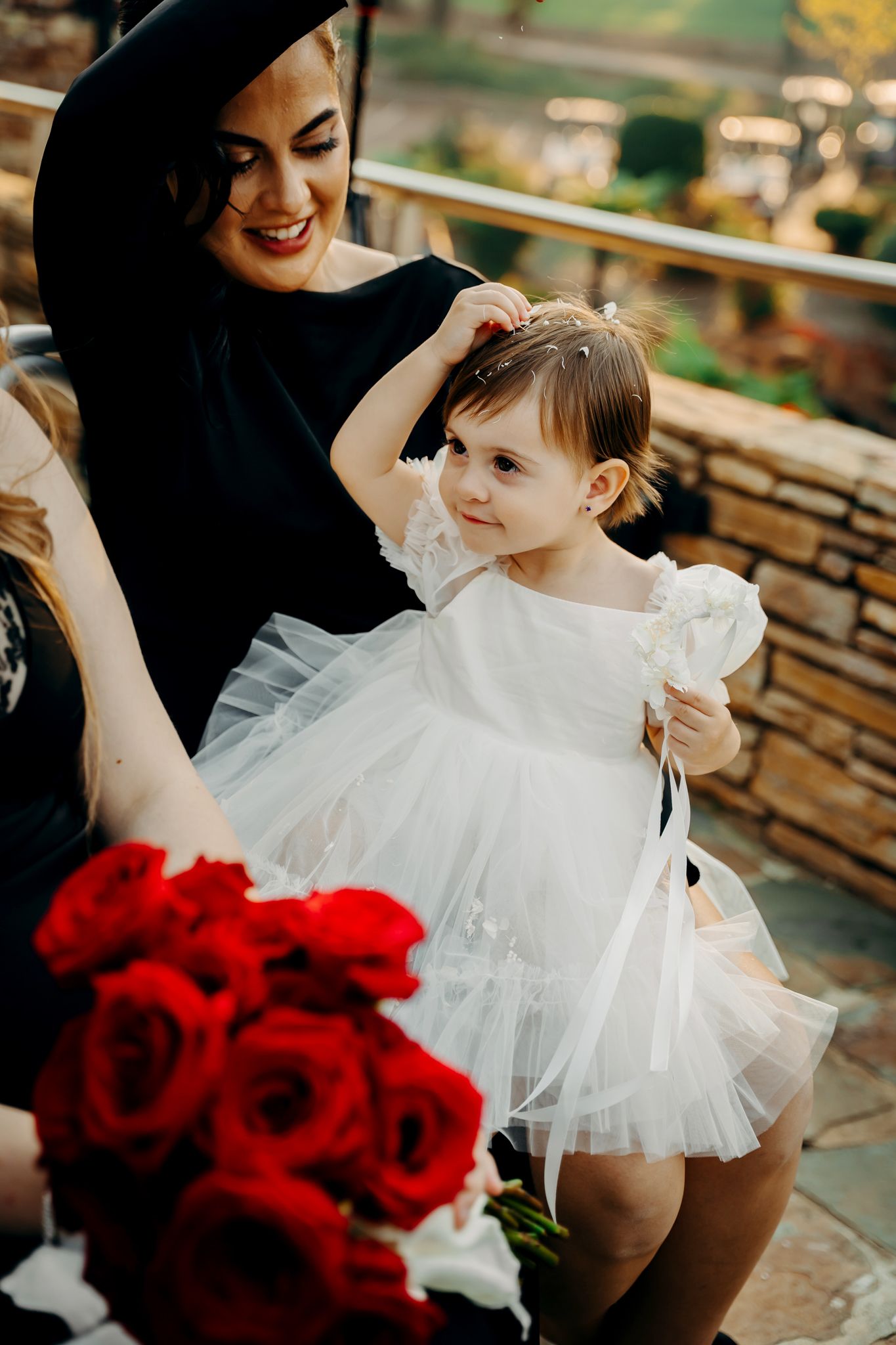 A touching moment in white tulle dress with vibrant red roses creating elegant contrast at an outdoor venue.