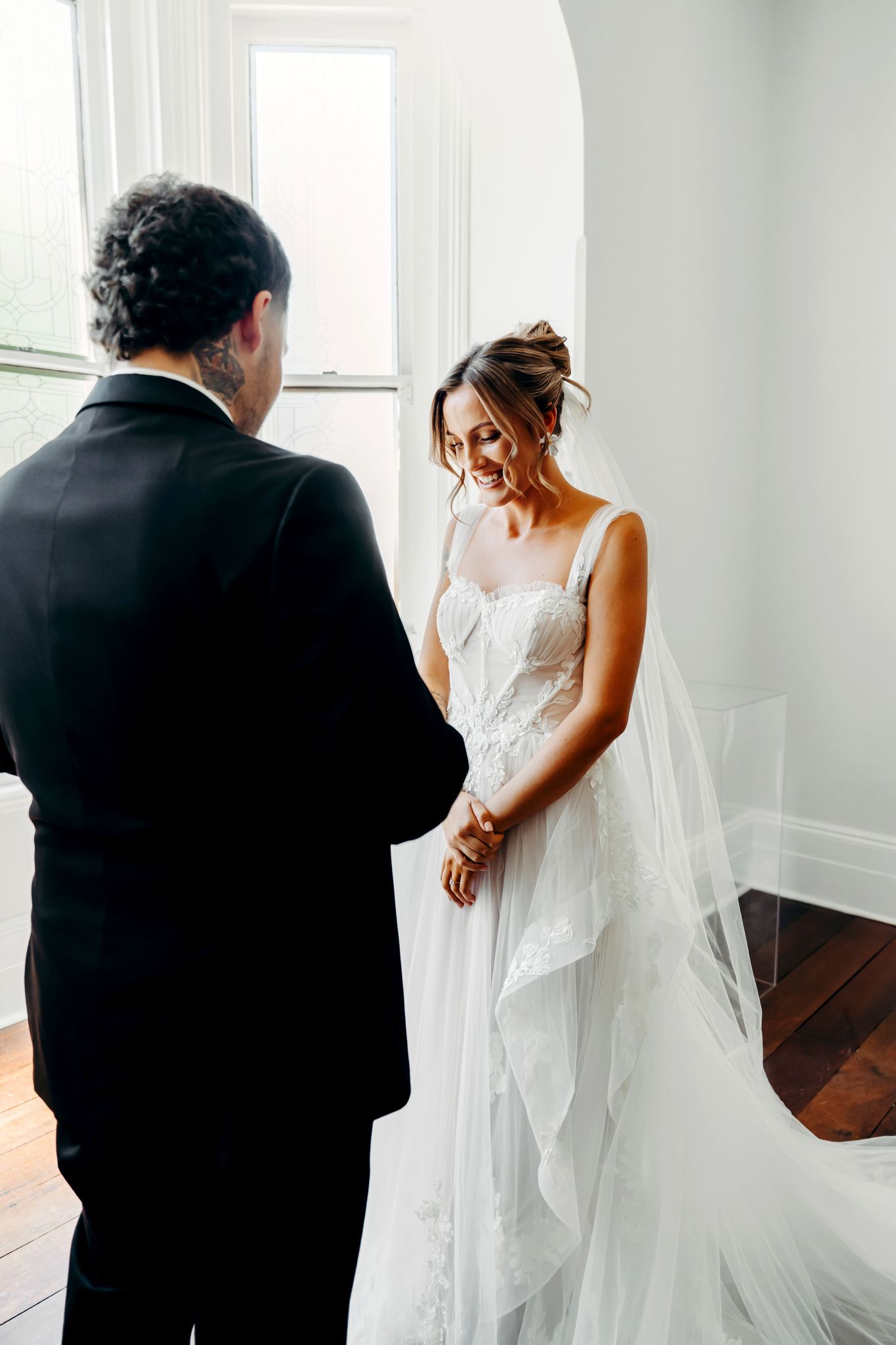 A bride in a flowing white dress and veil stands before someone wearing black during an intimate wedding moment.