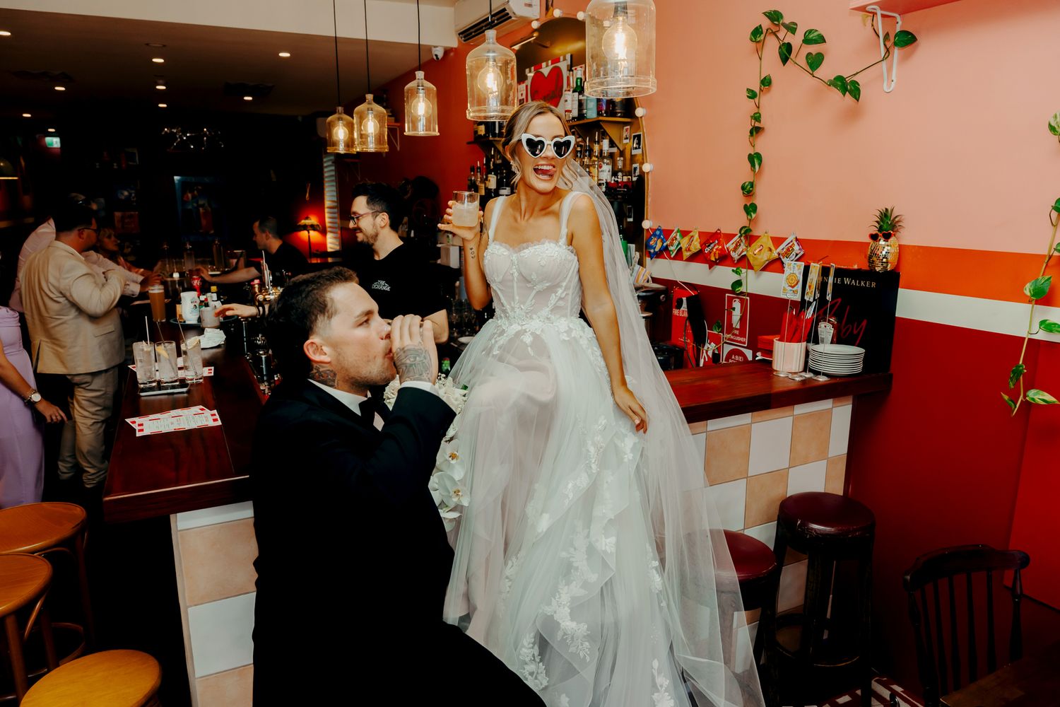 A couple celebrates their wedding at a retro-style diner with pink walls and pendant lighting.