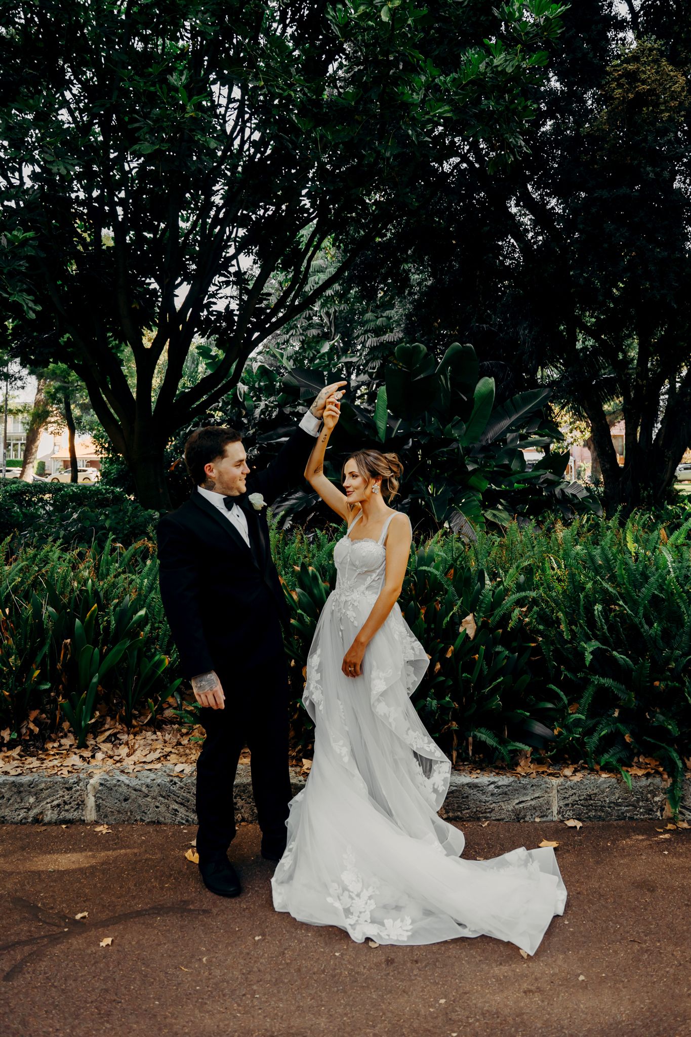 A romantic newlywed couple dancing together in a lush garden setting during their wedding celebration.