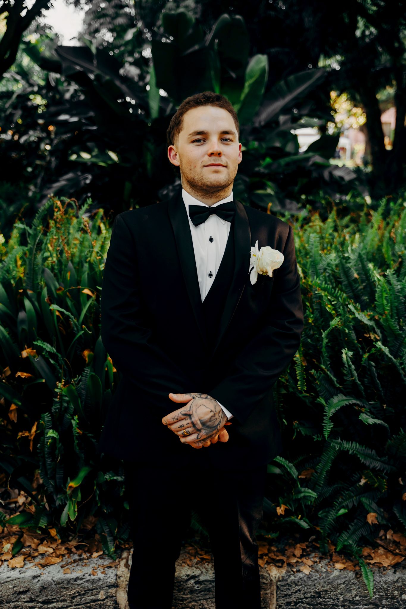 A formal wedding portrait among garden foliage with yellow flowers in the background.