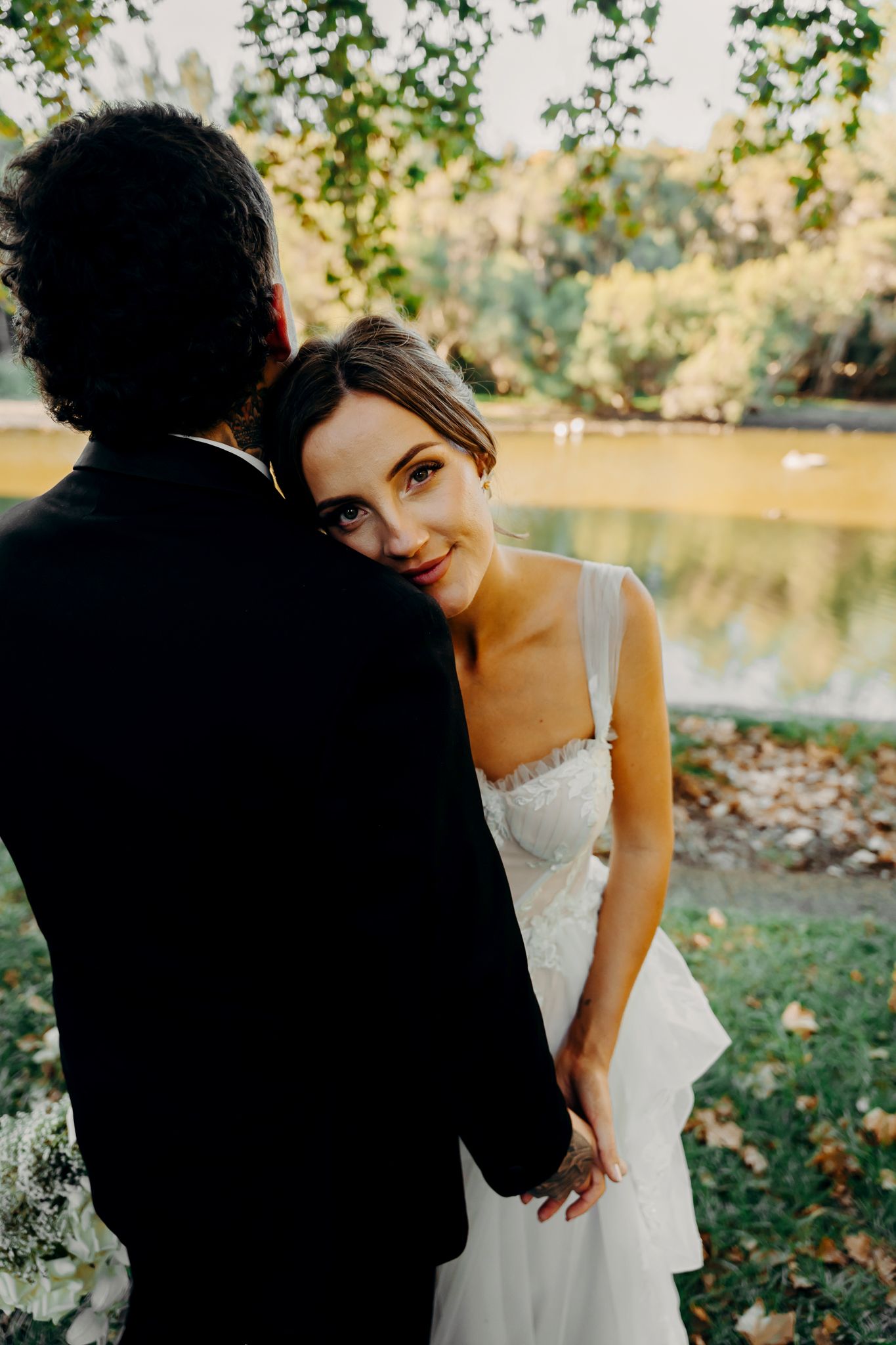 A candid moment between newlyweds standing by a lake during golden hour at their wedding celebration.