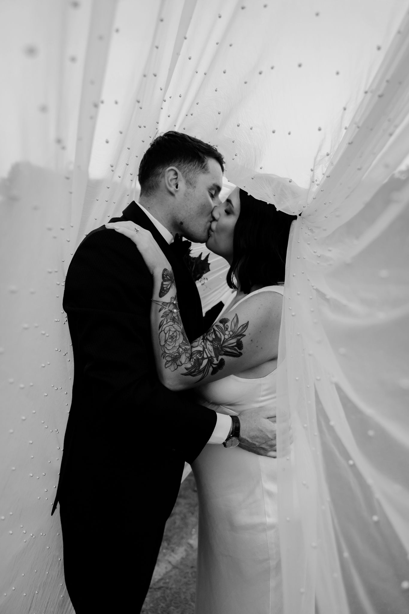 Black and white wedding photo of a romantic moment between a couple under flowing fabric and sparkles.