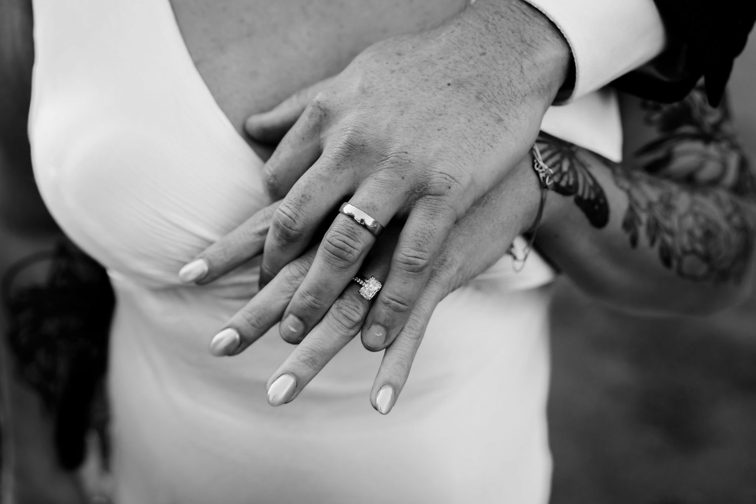 Closeup of hands showing wedding rings against white fabrics in black and white photograph.