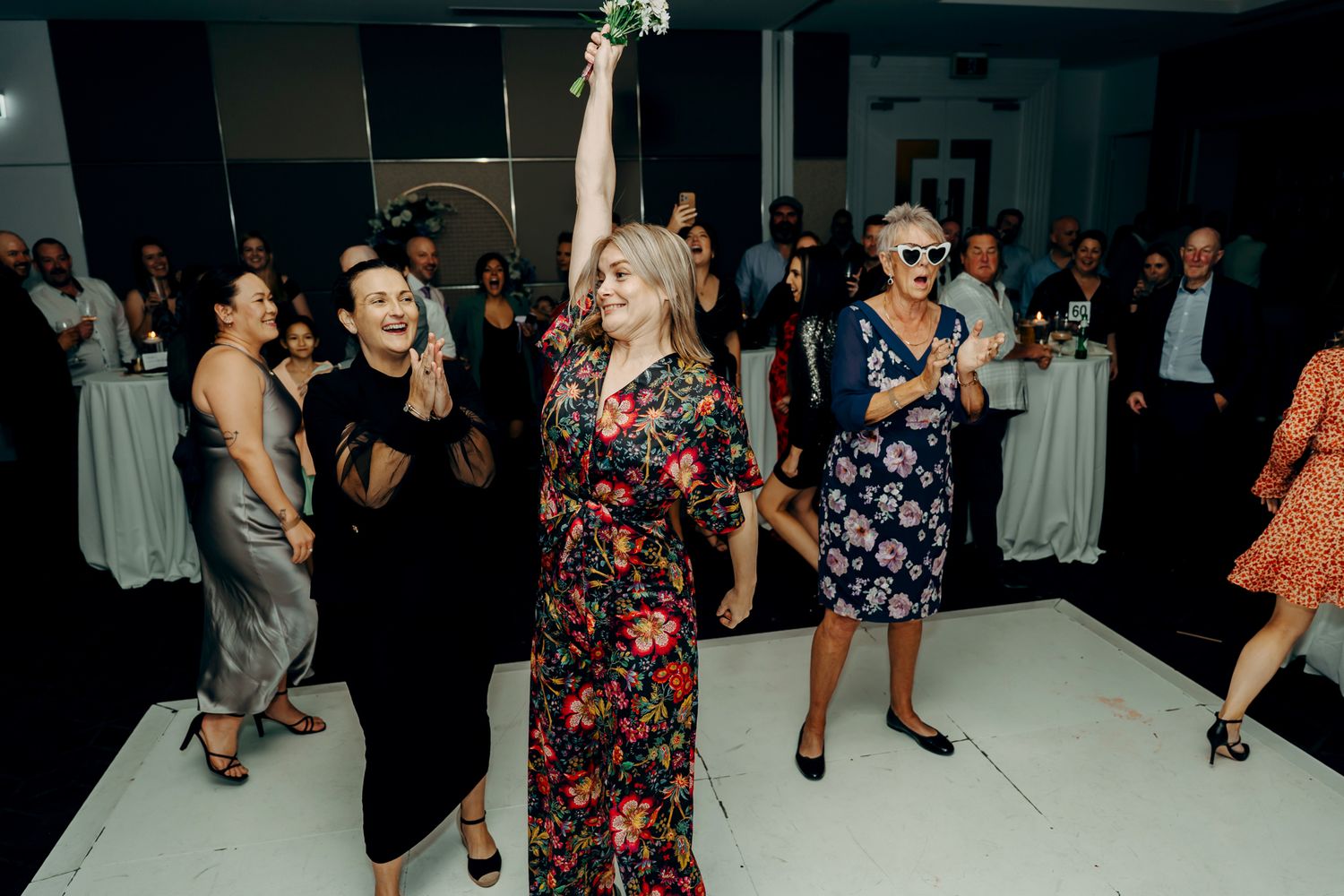 Wedding guests dance and celebrate on a dimly lit dance floor during a lively reception party.