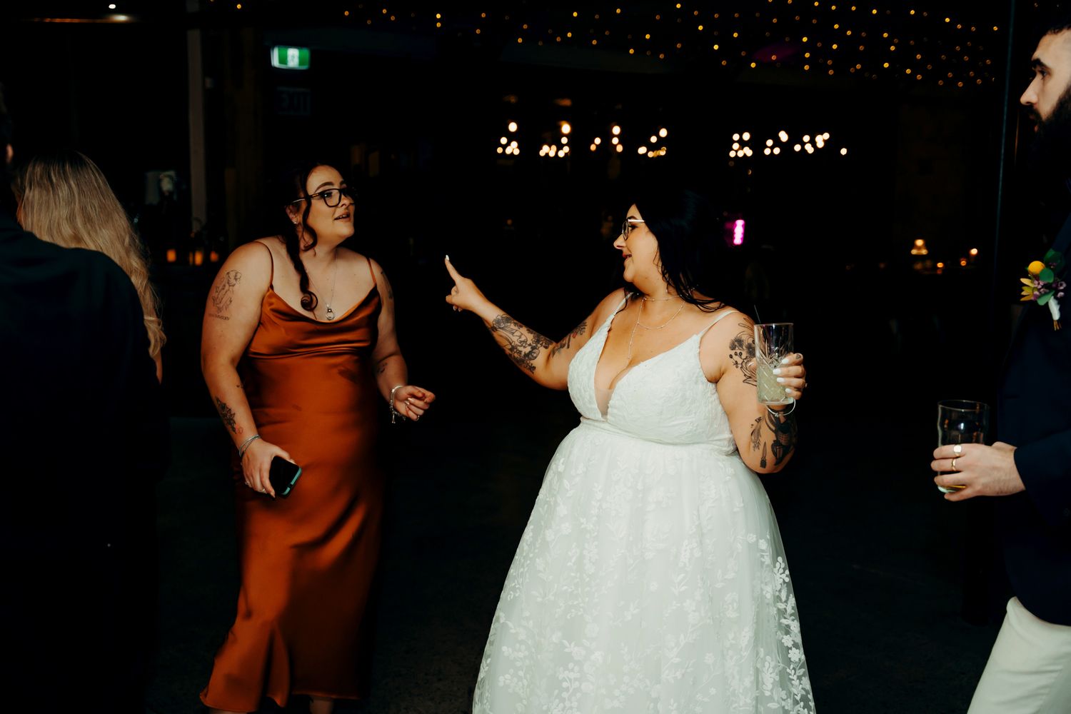 Wedding guests dance and celebrate together on a dark dance floor illuminated by party lights.