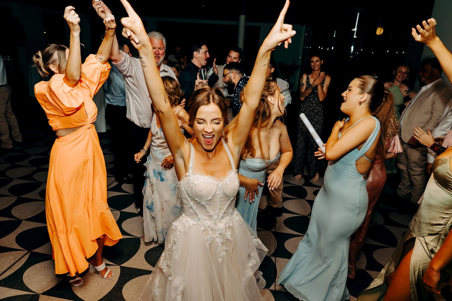 A joyous wedding reception with guests dancing and celebrating on a black and white checkered dance floor.
