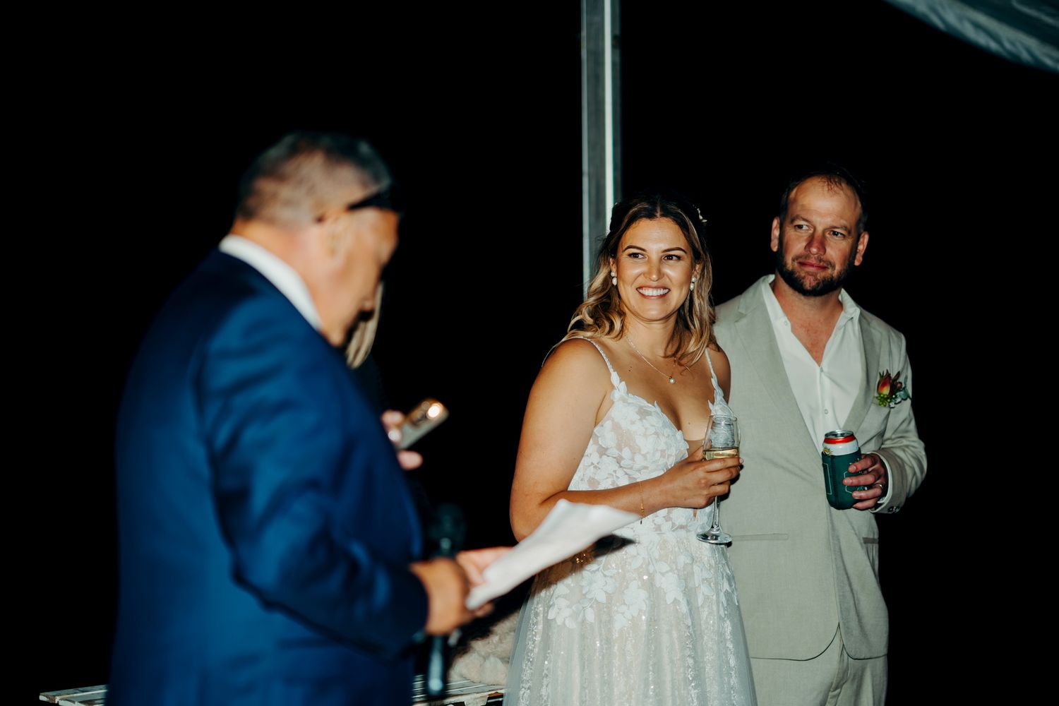Nighttime wedding reception scene with guests mingling under string lights in a festive outdoor setting.