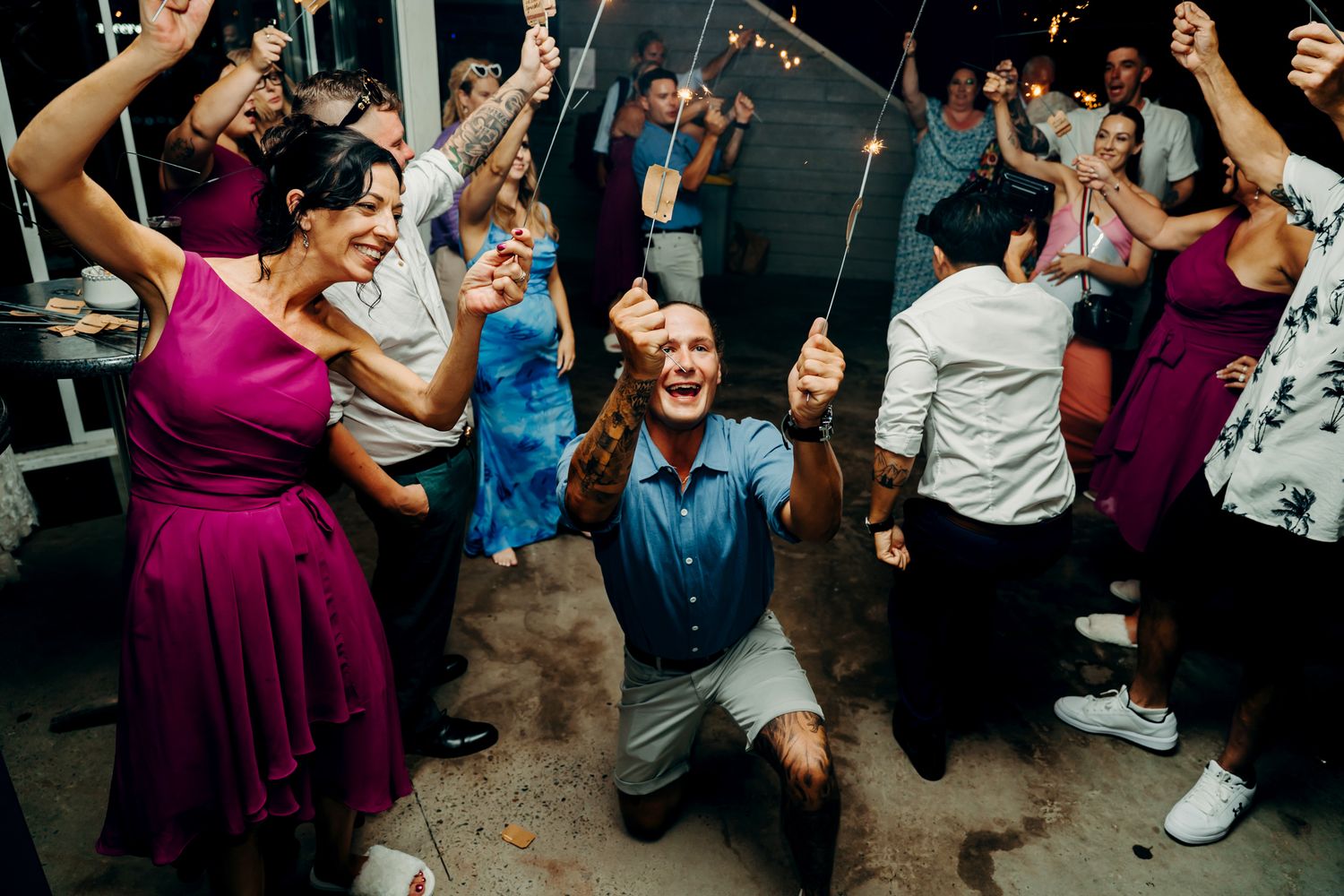Joyful wedding reception guests dancing and celebrating with sparklers at an evening party.