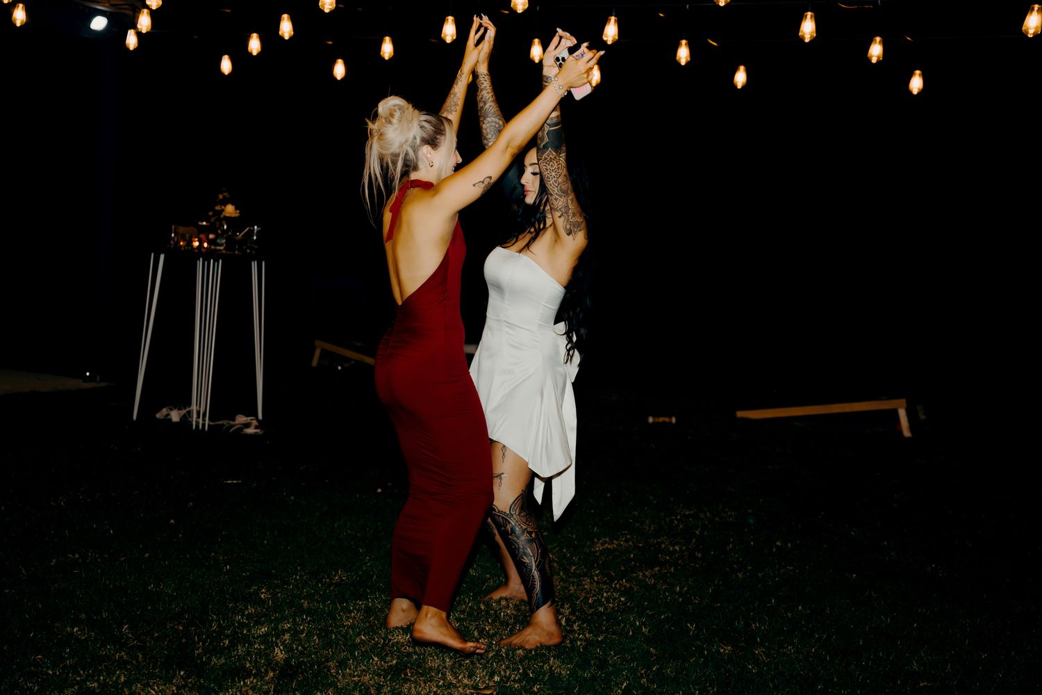 Couples dancing and celebrating at an outdoor nighttime wedding reception with string lights overhead.
