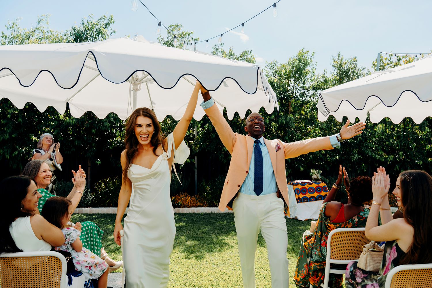 Joyful newlyweds celebrate their outdoor wedding reception under a striped tent with cheering guests.